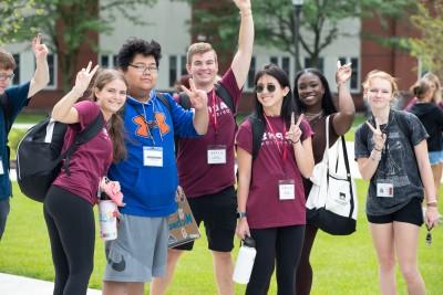 A group of happy students gather together and show the peace sign